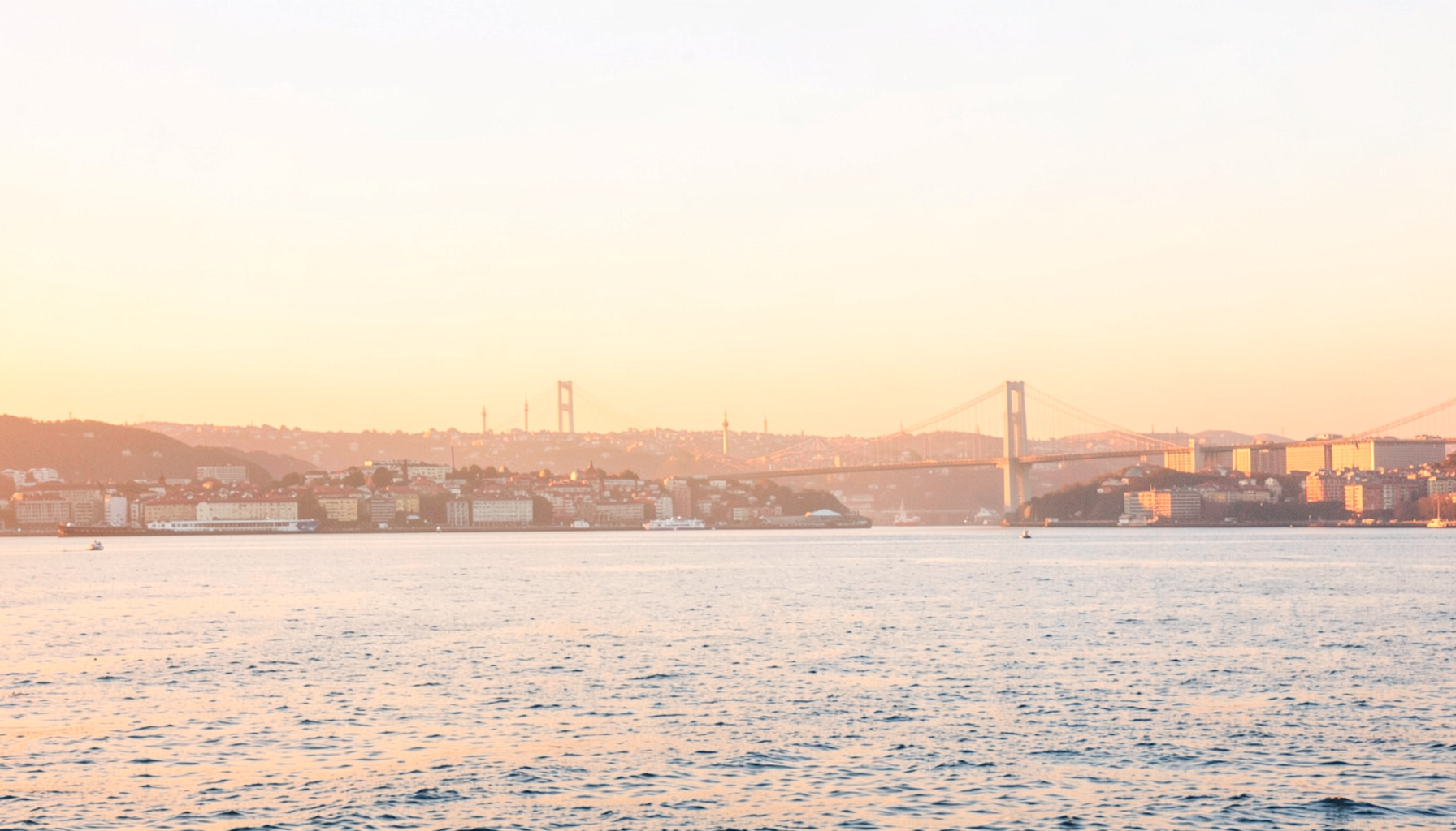 İstanbul silüeti, sıcak turuncu ve altın tonlarında akşam ışığı, Boğaz köprüsü ve yumuşak gökyüzü